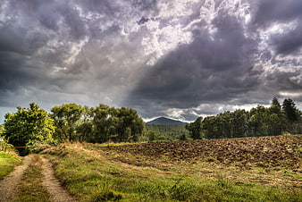 Dramatic storm clouds over rural landscape with path and mountain