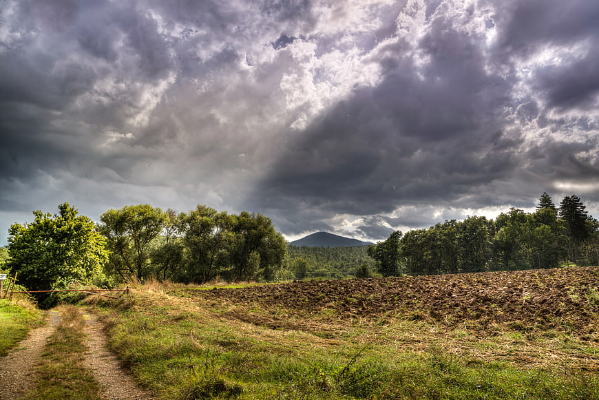 Dramatic storm clouds over rural landscape with path and mountain