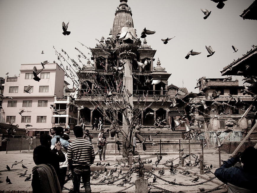 Sepia-toned temple square with flying pigeons and tourists