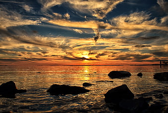Dramatic sunset over ocean with silhouetted rocks and clouds