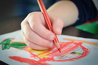 Close-up of a child's hand drawing with a red colored pencil