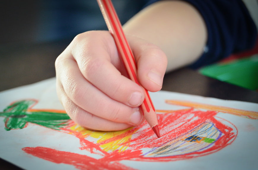 Close-up of a child's hand drawing with a red colored pencil