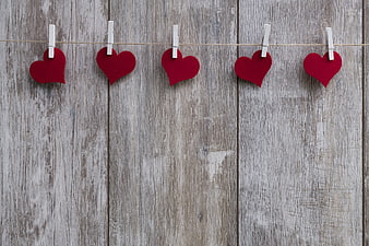 Red felt hearts hanging on clothesline against rustic wood background