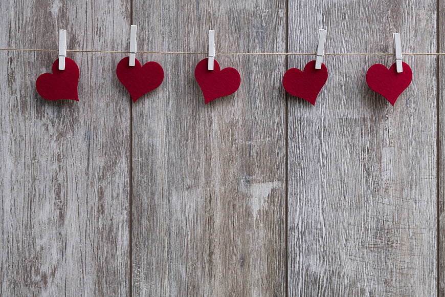 Red felt hearts hanging on clothesline against rustic wood background