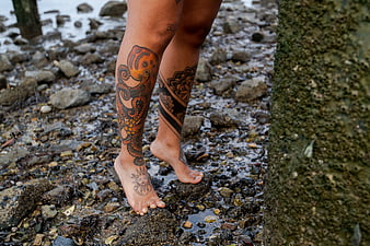 Barefoot Woman with Octopus and Mandala Tattoos Walking on Rocky Beach