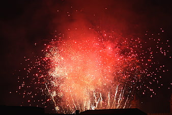 Vibrant red fireworks exploding over a dark city skyline at night