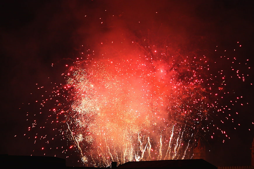 Vibrant red fireworks exploding over a dark city skyline at night
