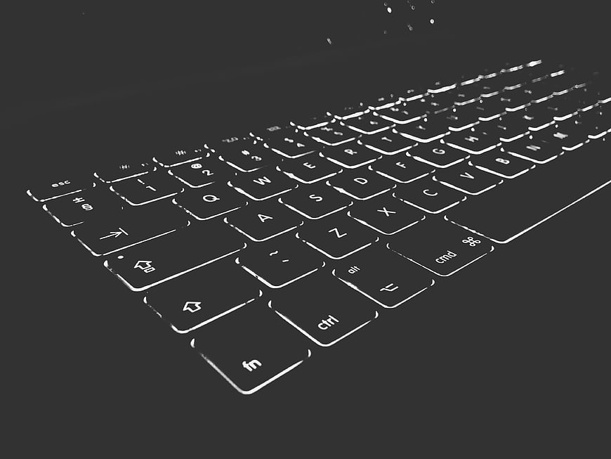 Black computer keyboard with white backlighting on dark background