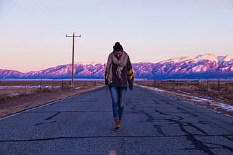 Woman Walking on Rural Road with Snowy Mountains at Sunset