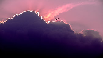 Silhouette of Airplane Flying Over Dramatic Purple Clouds at Sunset