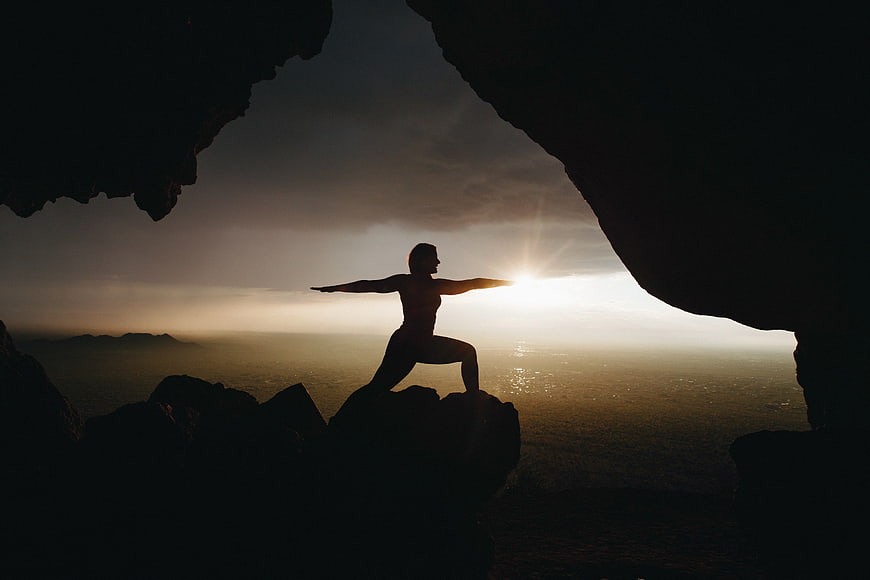 Silhouette of woman doing yoga in cave at sunset