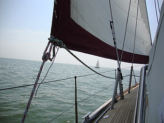 Sailing boat deck view with red and white sail on ocean