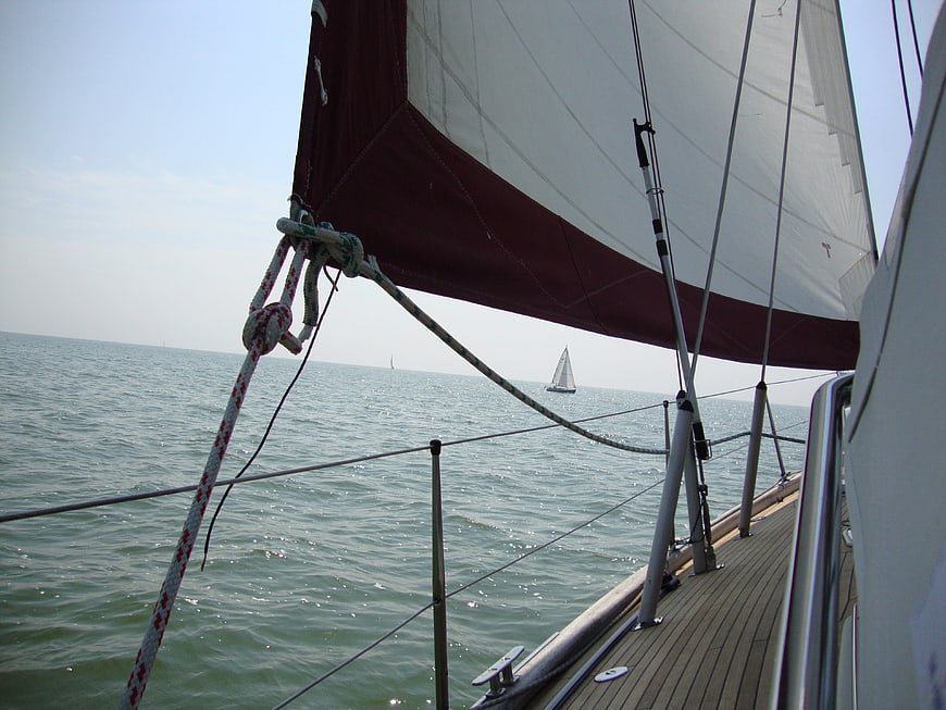 Sailing boat deck view with red and white sail on ocean