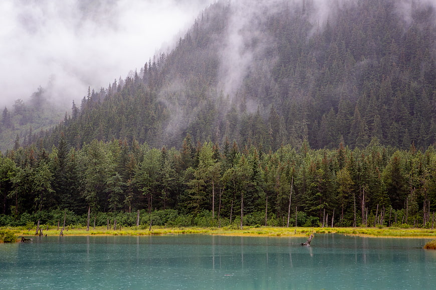 Misty turquoise lake with forested mountain landscape