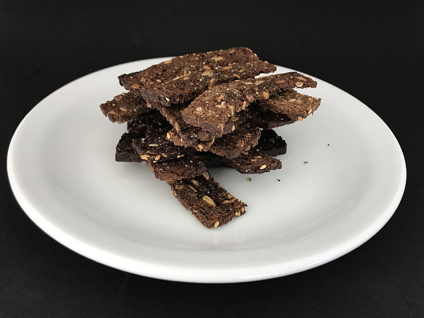 Stack of dark rye bread chips on white plate