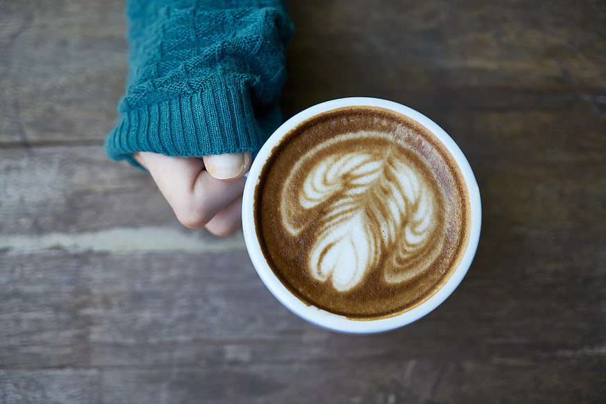 Top View of Hand Holding Latte with Leaf Art