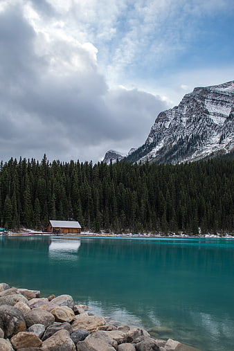 Serene turquoise lake with wooden cabin and snowy mountains