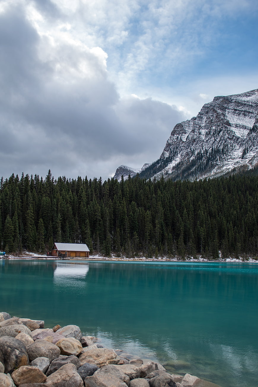 Serene turquoise lake with wooden cabin and snowy mountains