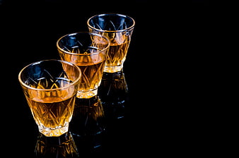 Three crystal glasses filled with amber liquor on a black reflective surface
