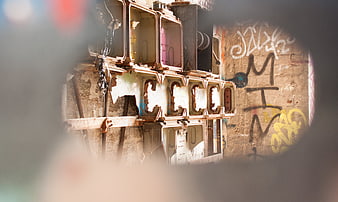 Rusty electrical boxes on graffiti wall seen through hole