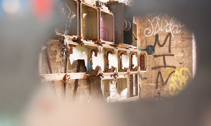 Rusty electrical boxes on graffiti wall seen through hole