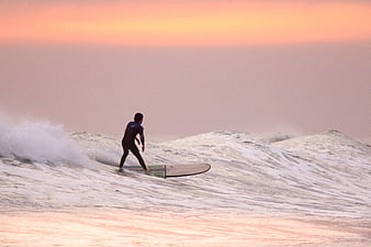 Surfer riding ocean wave during pink sunset