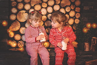 Two young girls in red pajamas drinking milk by a Christmas tree