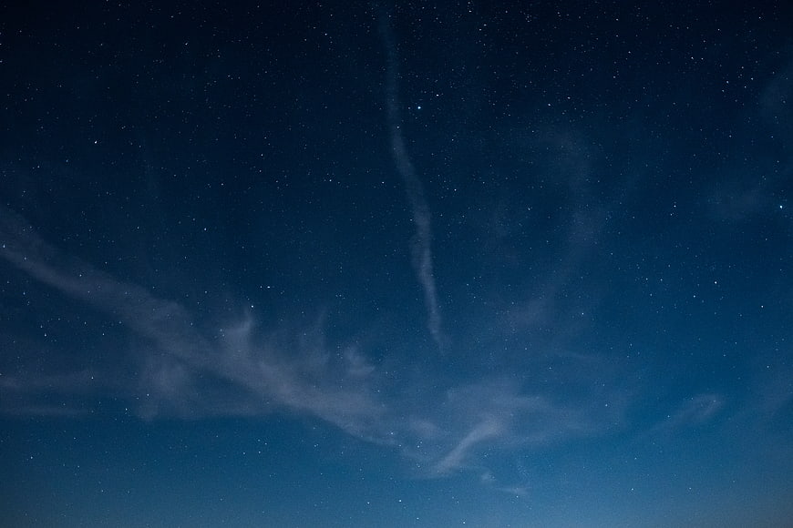 Starry night sky with wispy clouds and deep blue gradient