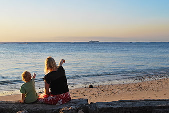 Mother and child pointing at ship on ocean horizon at sunset