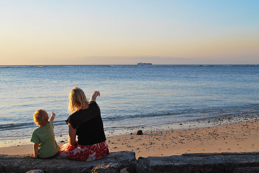 Mother and child pointing at ship on ocean horizon at sunset