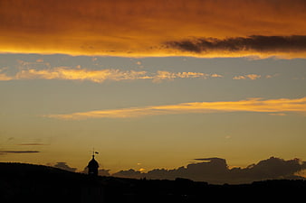 Silhouette of church tower against dramatic golden sunset sky