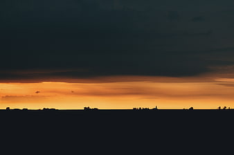 Dramatic sunset silhouette landscape with dark clouds and orange sky