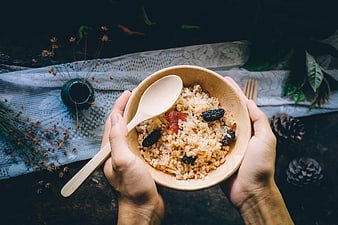Hands holding wooden bowl of rice with dried fruit