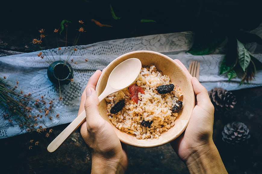 Hands holding wooden bowl of rice with dried fruit