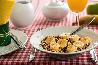 Healthy breakfast bowl with granola and sliced bananas on checkered tablecloth