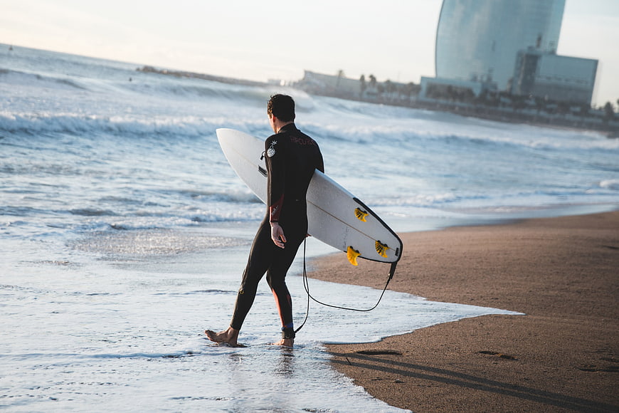 Surfer walking on beach with surfboard at sunset
