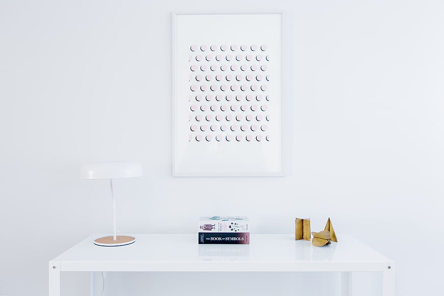 Minimalist white desk with lamp, books, and framed art