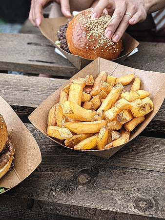 Close-up of hands holding burger with fries on wooden table