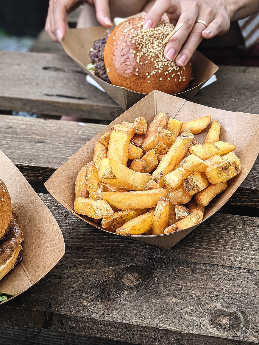 Close-up of hands holding burger with fries on wooden table