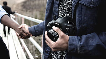 Photographer holding Canon camera shaking hands on bridge
