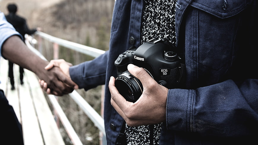 Photographer holding Canon camera shaking hands on bridge