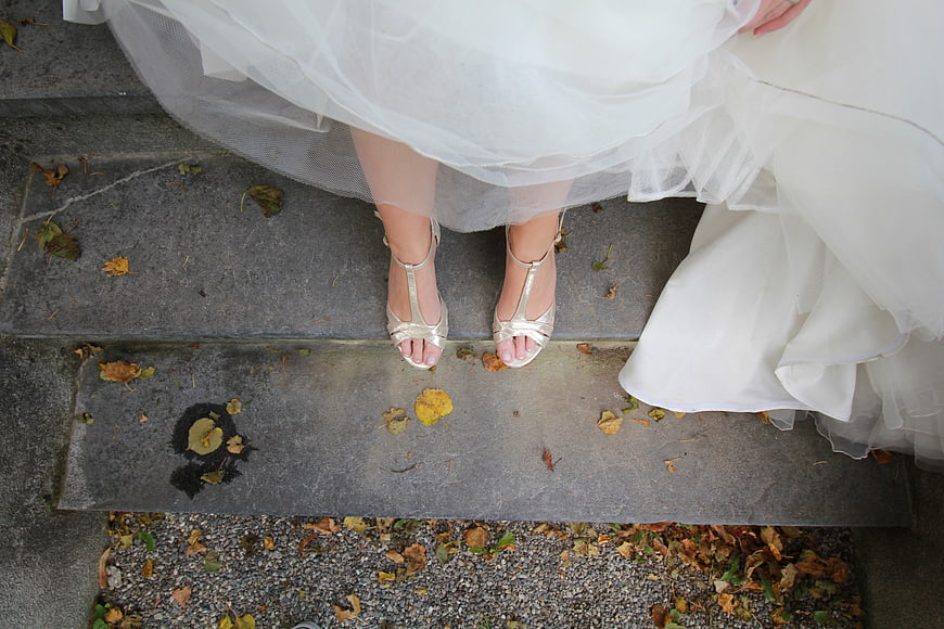 Bride's feet in silver heels on stone steps with autumn leaves