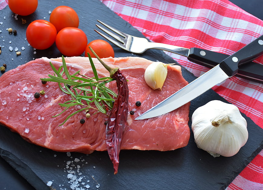 Raw beef steak with rosemary, garlic, and tomatoes on slate