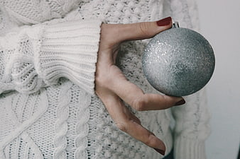 Woman holding silver glitter Christmas ornament in white sweater