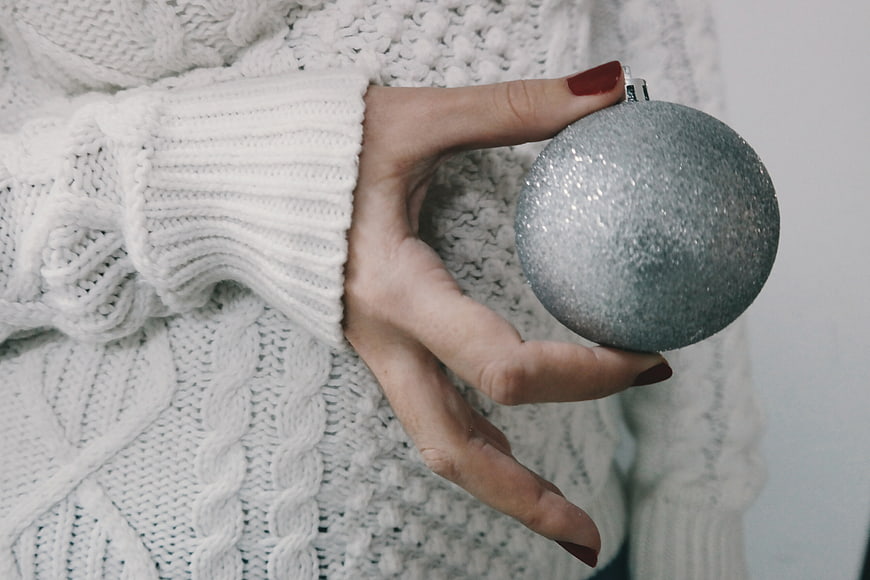 Woman holding silver glitter Christmas ornament in white sweater