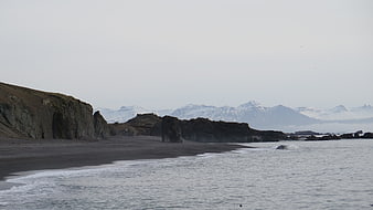 Dramatic black sand beach with cliffs and snowy mountains