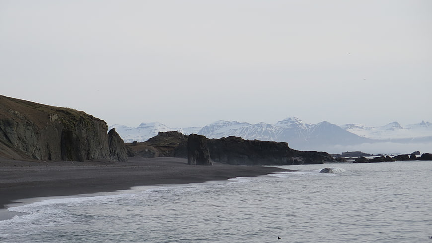 Dramatic black sand beach with cliffs and snowy mountains