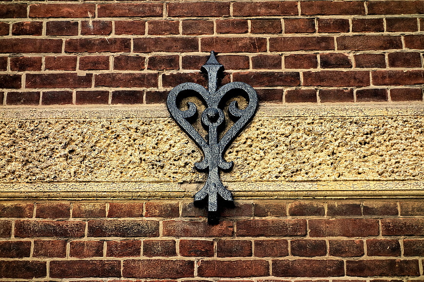 Vintage wrought iron fleur-de-lis on textured brick wall