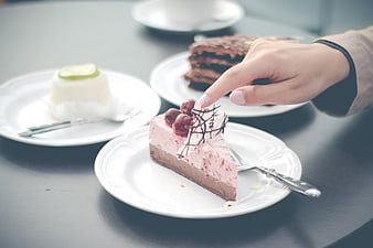 Hand Touching Strawberry Cheesecake Slice on White Plate
