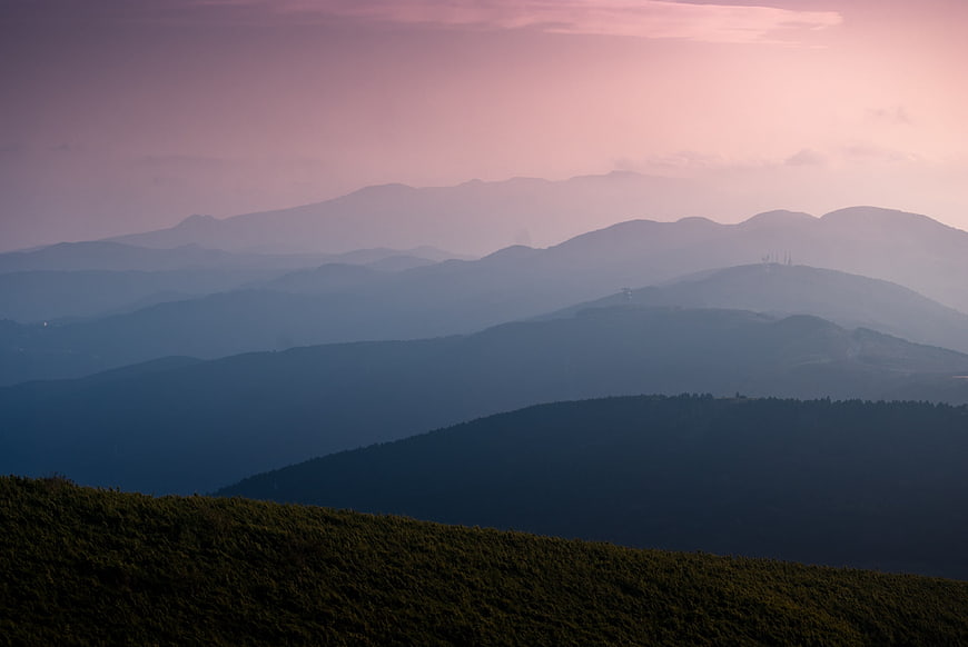 Layered mountain ridges in atmospheric haze with pink sunset sky